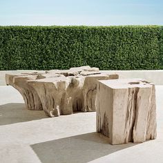 two stone benches sitting on top of a cement floor next to a green hedge covered wall