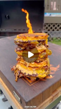 a stack of food sitting on top of a wooden table next to a fire pit