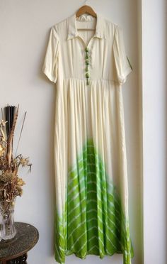 a green and white dress hanging on a wall next to a vase with dried flowers