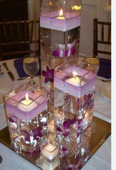 several square candles are stacked on top of each other with purple flowers and orchid petals