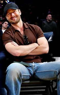 a man with his arms crossed sitting on a bench in front of other people at a basketball game