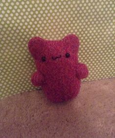 a red teddy bear sitting on top of a carpeted floor next to a wall