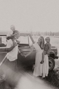 a black and white photo of a family standing in front of a car