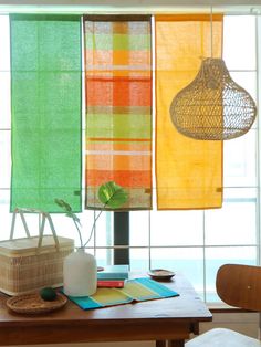 three different colored towels hanging from the ceiling in front of a table with a basket and vase on it