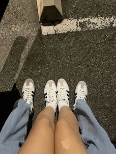 two people sitting on the ground with their legs crossed and one person wearing white sneakers