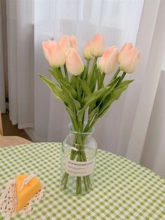 a vase filled with pink tulips sitting on top of a green and white checkered table cloth