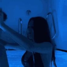 two people standing in a room with blue lighting on the walls and floor, one person is holding something up to her head