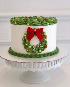 a white cake decorated with holly wreaths and a red bow is sitting on a pedestal