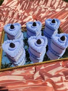 there are four blue cakes in the shape of hearts on a gold tray with pink satin