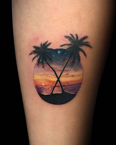 a couple of palm trees in a circle tattoo on the left calf side, with an ocean sunset behind it