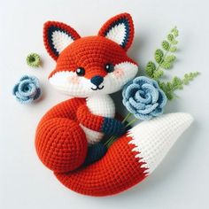 a crocheted red fox with flowers on it's back sitting next to another stuffed animal