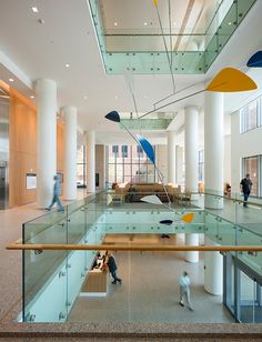 people are walking around in the lobby of an office building with glass railings and colorful sculptures