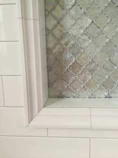 a bathroom with white tile and a window in the wall that has an intricate pattern on it