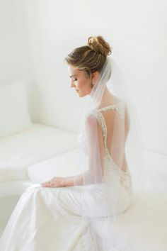 a woman sitting on top of a white couch wearing a wedding dress with a veil over her head