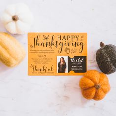 an orange thanksgiving card sitting on top of a table next to two small pumpkins