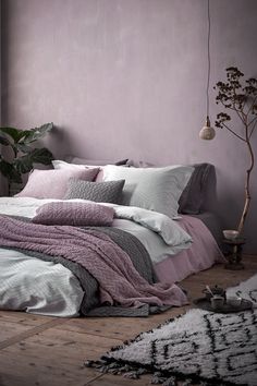 a bed covered in pink and grey blankets next to a window with potted plants