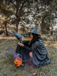 a woman and child dressed up as witches sitting on the ground in front of trees