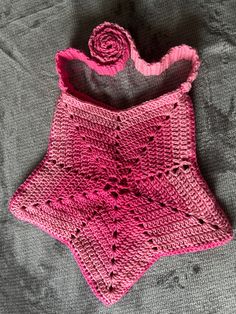 a pink crocheted shawl laying on top of a gray blanket next to a flower