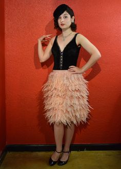 a woman standing in front of a red wall wearing a black top and pink feather skirt