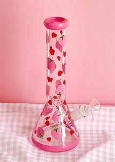 a pink vase with strawberries on it sitting on a checkered table cloth next to a pink wall