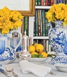 two blue and white vases with yellow flowers in them sitting on a table next to silverware