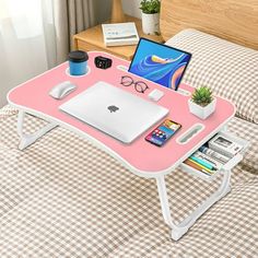 a pink tray with a laptop, glasses and other items on it sitting on a bed