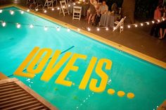 people sitting at tables around a pool with lights strung over the edge and an overhead sign that says oveis