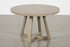 a round wooden table sitting on top of a cement floor next to a white wall