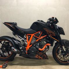 an orange and black motorcycle parked next to a white wall in a room with concrete floors