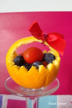 an orange decorated with berries and a bow on top of a stand in front of a pink wall