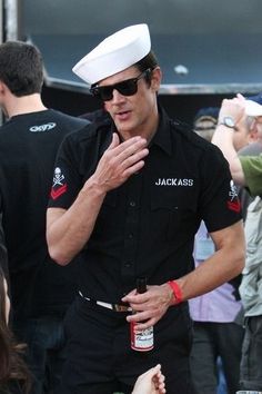 a man in a sailor's uniform is talking to someone on the street while people are standing around him