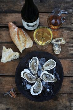 oysters and bread on a black plate next to a bottle of wine with ice