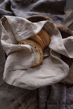 a basket filled with sliced bread on top of a wooden table next to a gray blanket