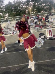 two cheerleaders in maroon and white outfits dancing on the sidelines at a football game