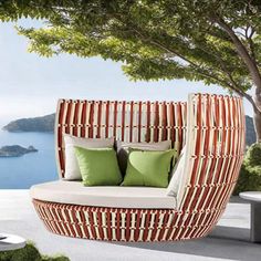 an outdoor day bed with green pillows on the top and bottom, next to a tree