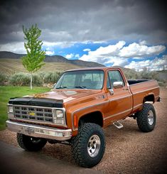 an orange pick up truck parked on top of a dirt road