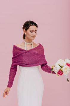 a woman in a white dress holding a bouquet and wearing a purple sweater over her shoulder