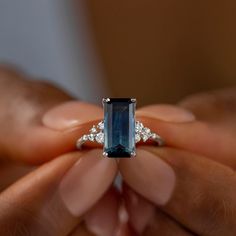 a woman's hands holding a ring with an emerald and diamond set in it