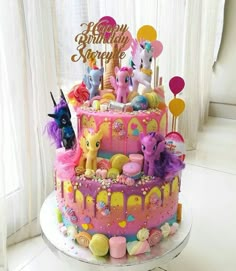 a birthday cake decorated with pink icing and rainbow ponys, balloons and confetti