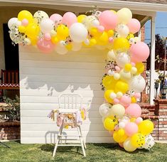 a bunch of balloons that are in the grass near a house with a lawn chair