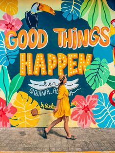 a woman walking in front of a colorful wall that says good things happen