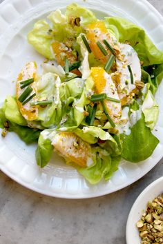 a white plate topped with lettuce and oranges next to a bowl of granola