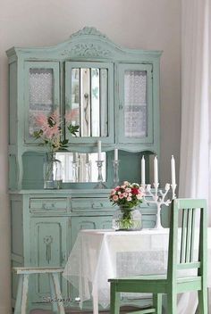 a dining room table and chairs with flowers in vases on the china cabinet next to it