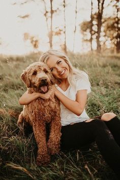 a woman is sitting in the grass with her dog and she has her arms around her chest