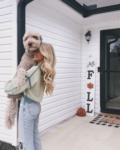 a woman holding a dog in her arms while standing on the front steps of a house