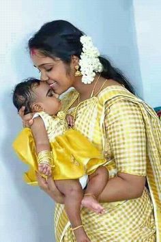 a woman holding a baby in her arms and smiling at the camera while wearing a yellow sari