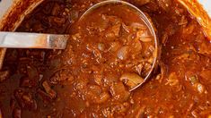 a spoon in a pot filled with chili and meat sauce on top of a table