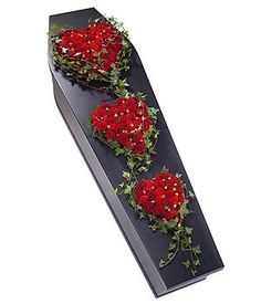 three red roses arranged in the shape of hearts on a black tray with greenery