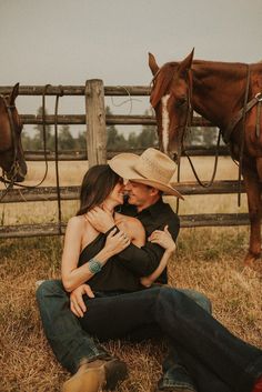 a man and woman sitting on the ground in front of horses with their heads close to each other