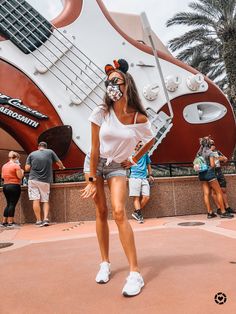 a woman standing in front of a giant guitar shaped building with people walking around it